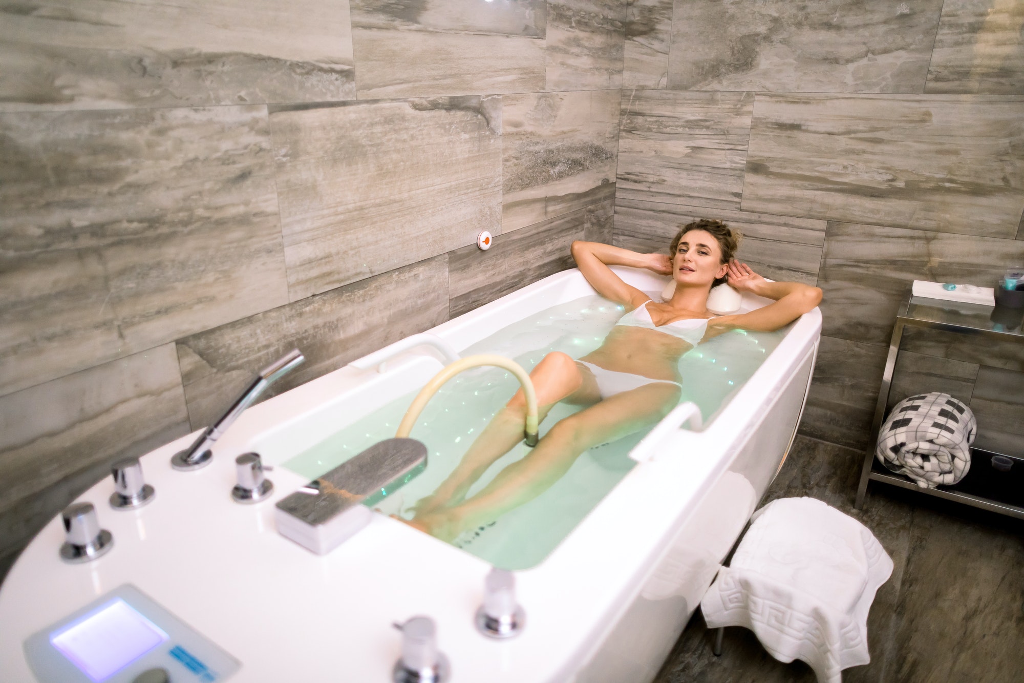 Young beautiful woman receives hydro massage and medical treatments for relaxation in modern spa